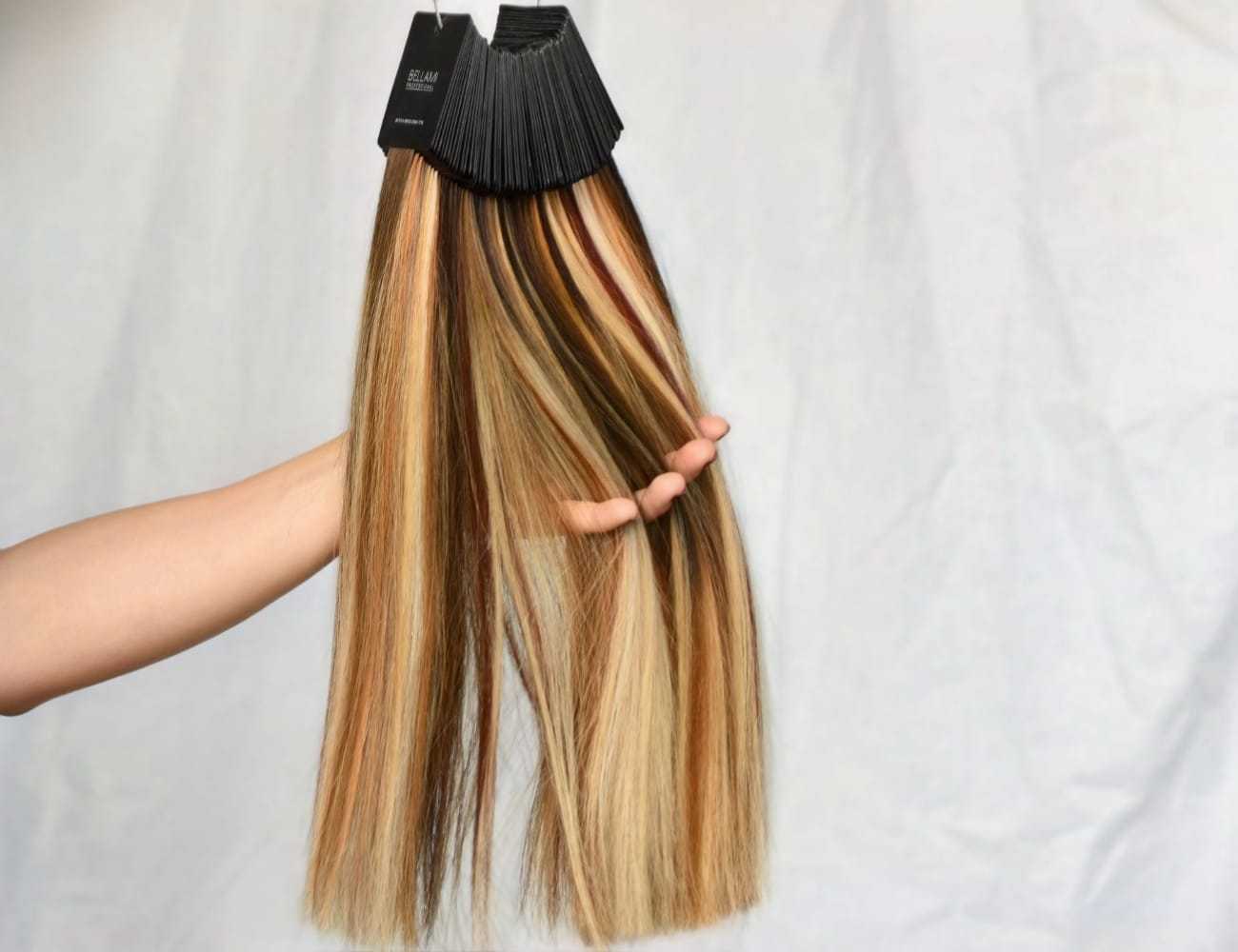 Hand holding colorful hair extension samples against a neutral background.